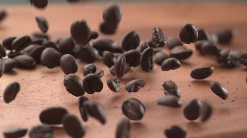 Kaffeebohnen, die in Super auf eine Holzoberfläche fallen.
Auf