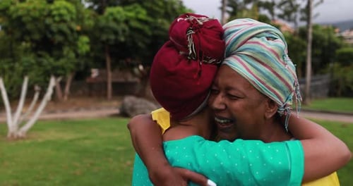 Women share an emotional hug in a park setting