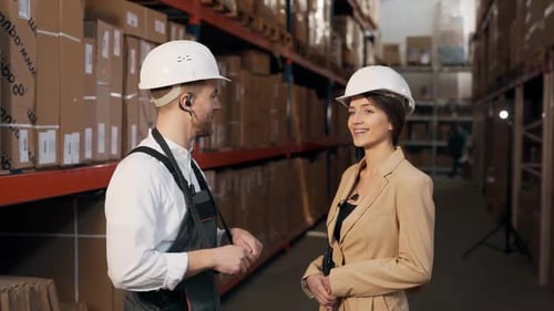 Pleasant young man conducts a tour of a young woman in a business suit on the territory of the wareh