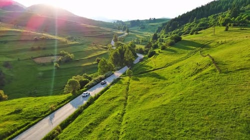 A Road Passes Hills Covered with Spruce Forests and Meadows Against a Cloudy Sky