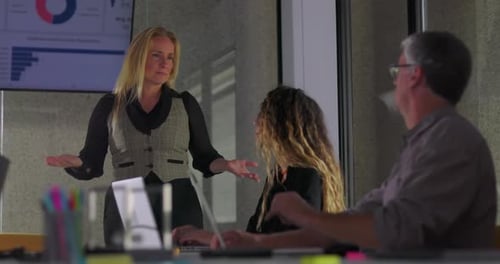 Blonde businesswoman giving presentation to team while standing in office meeting room with data