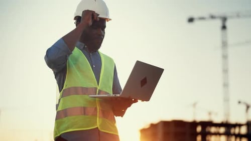 Moderne Innovation im Bauwesen: Porträt eines afroamerikanischen Baumeisters beim Bauleiter mit Laptop