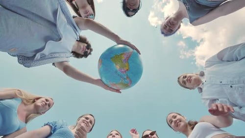 Eine Gruppe junger Freunde steht draußen im Kreis und hält einen Globus über ihren Köpfen