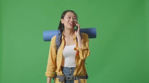 Asian Female Hiker Talking On Smartphone And Looking Around While Walking On Green Screen