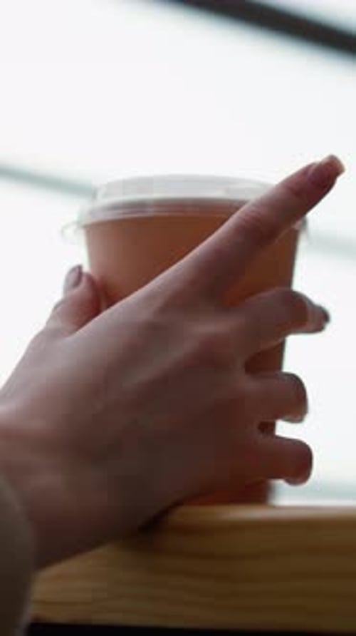 Closeup of Woman Hand Tapping Beverage Cup on Wooden Table in Cozy Modern Cafe