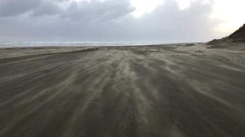 Beach sand streaming in the wind under a cloudy sky on Ninety Mile Beach Northland New Zealand