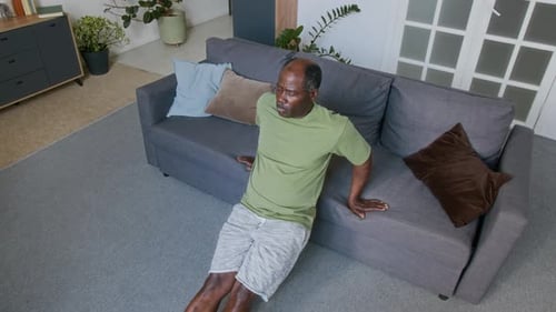 Middle Aged Man Exercising at Home on Sofa