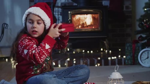 Excited Girl Opening Gift By Fireplace On Christmas