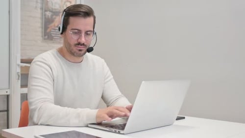 Young Man with Headset Working on Laptop in Call Center