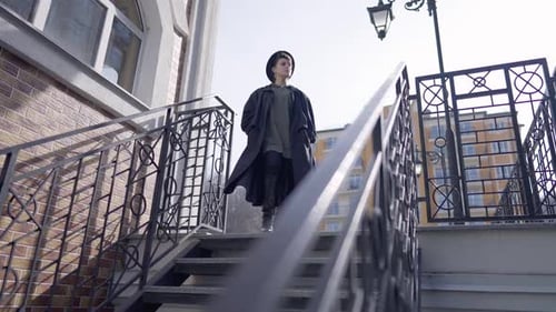 Young Gorgeous Woman in Highheels and Hat Standing Upstairs with Wind Blowing Cloak in Slow Motion