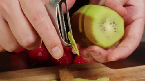 Hands Peel Kiwi on Cutting Board Close Up