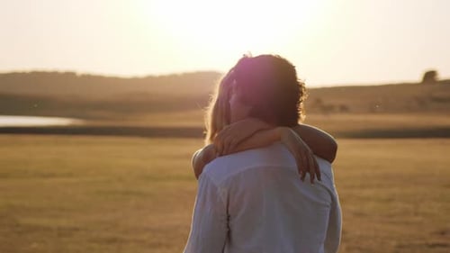 Hugged couple enjoy their love in a meadow under a golden sunset - Medium shot slow motion