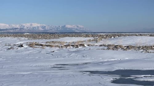 Aerial Drone Gliding Low Above Snow Covered Shoreline of Ocean in Winter Time