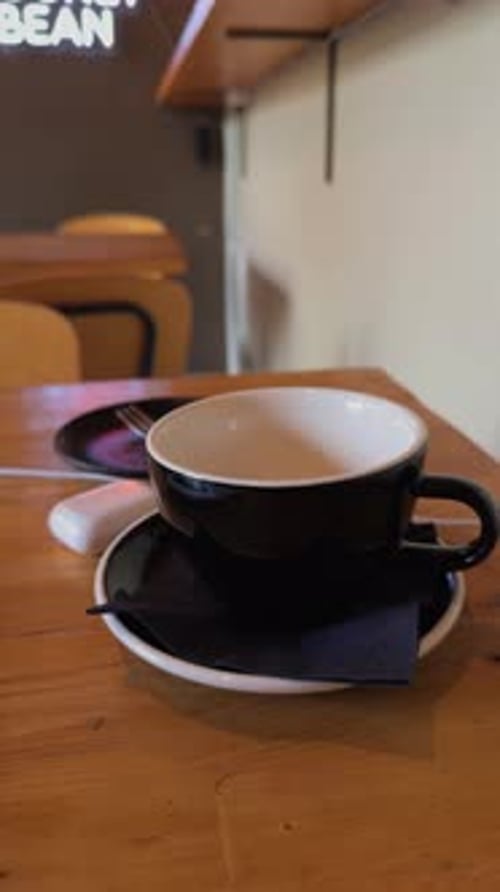 A Charming Black Coffee Cup is Placed on a Rustic Wooden Table in a Cozy Cafe Setting Ideal for