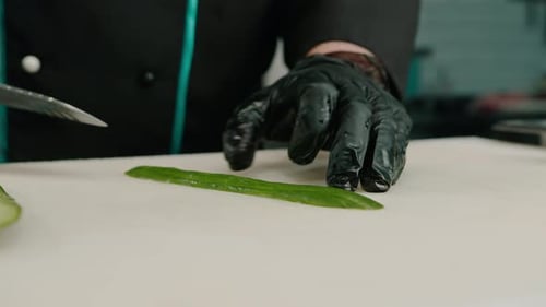 Close-up of a sushi maker in gloves cutting a cucumber with a professional kitchen knife