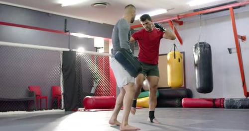 Vielfältiger männlicher Trainer und Auszubildender, der Knieschläge und Jabs im Ring mit Coach Raising Pads durchführt