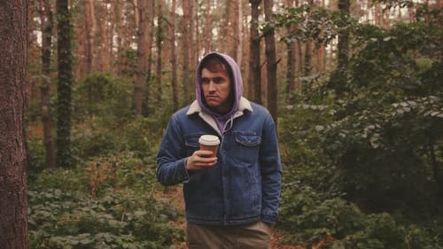 Young Man in Warm Clothes Drinking Coffee From Paper Cup Standing in Forest