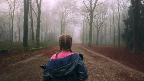 Young Girl with Braid Exploring Foggy Forest Trail during Morning Walk