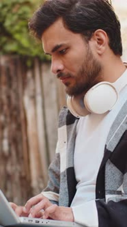 Indian Young Man Freelancer Sitting on Street Using Laptop Typing Working Online Distant Job Outdoor