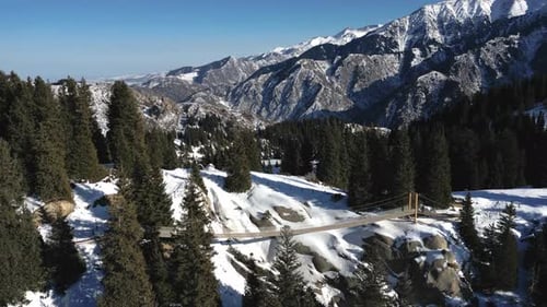 Aerial View of a Wooden Suspension Bridge Nestled Among a Snowcovered Gorge and Pine Trees with the