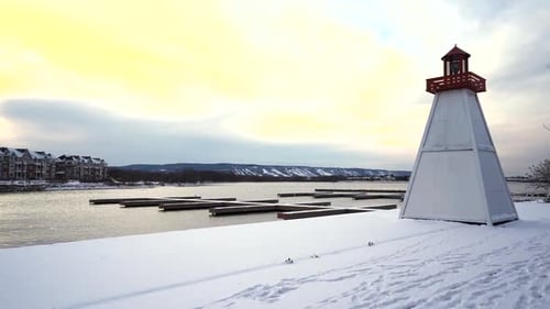 View of a lighthouse next to a frozen harbor with Blue Mountain ski hill in the distance.