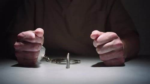 Close-up of a prisoner's hands while he sits calmly handcuffed to a table in an interrogation room,