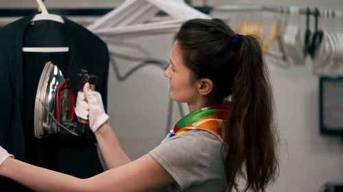 Close Up Professional Dry Cleaning Young Girl Irons a Black Sweater on Hanger with Steam
