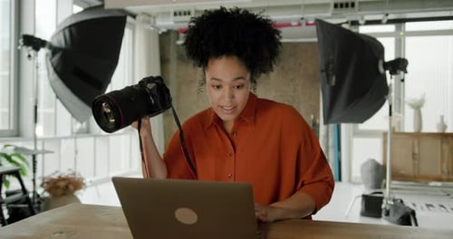 African American Female Photographer sitting in her Studio checking Camera and using Laptop
