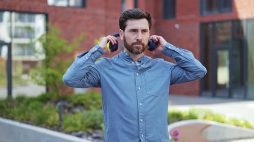 Man Putting On Headphones and Smiling in City
