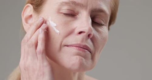 Woman Applies Cream to Face Smiling Close Up