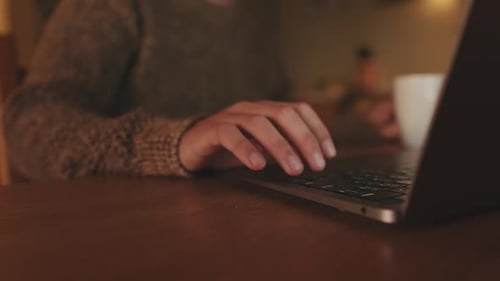 Close-up of the hands of an unrecognizable young male drinking coffee from mug while using laptop