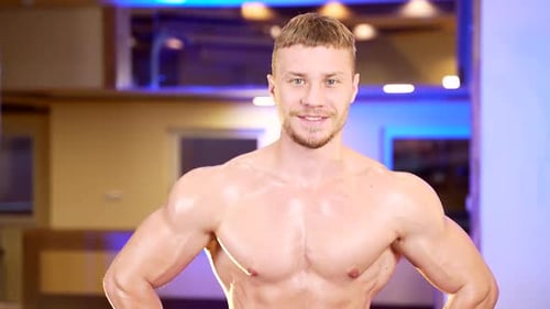 Close up portrait of a confident muscular shirtless bodybuilder guy looking at camera. Young strong