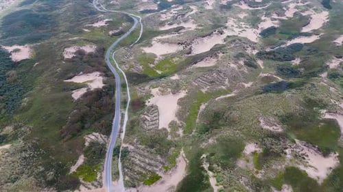 Aerial view of a coastal landscape with lush greenery, sandy dunes, and a winding road running