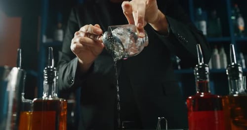 A professional bartender is preparing an alcoholic cocktail with ice cubes to customers at the bar
