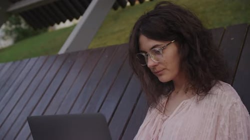 Handheld Close Up of a Curly Caucasian Woman Working on Her Laptop Computer in a Park