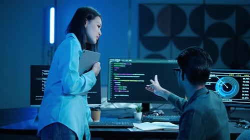 Two Asian software engineers collaborate in a office. Male programmer points at code on the computer