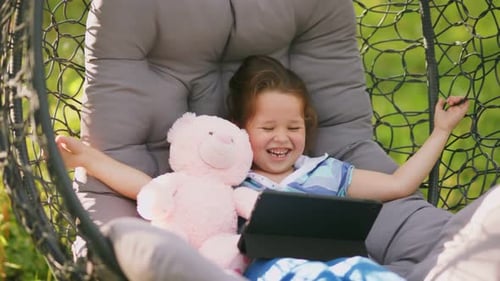 Girl Sits in a Rocking Chair Cocoon with Looks at the Tablet