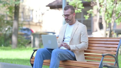 Man Types on Laptop on Park Bench Outdoors