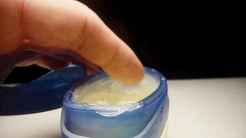 A blue jar of vaseline is on the table, I stick my finger in there and spread a little vaseline on.