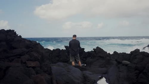 Man Standing on Rocky Shore Overlooking Turbulent Ocean Waves