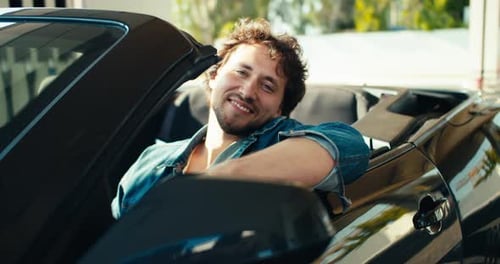 A Young Brunette Guy Looks Out of a Dark Gray Convertible Smiles and Looks at the Camera