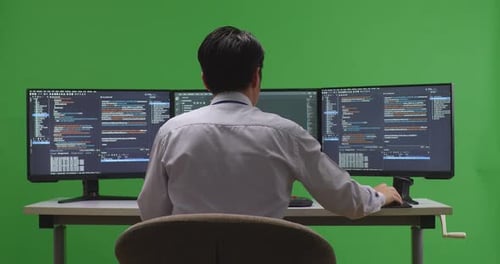 Back View Of Asian Man Developer Using Computer To Write Code With Multiple Screens In Green Screen