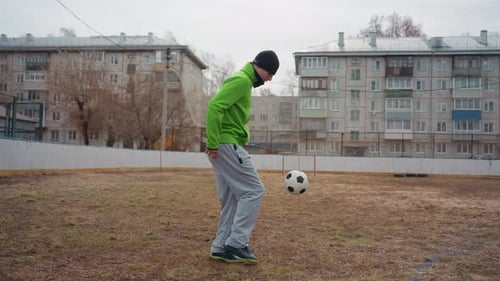 White Male Practicing Trick Kicks on Small Urban Field Nimble Footwork and Balance Casual Grey Pants