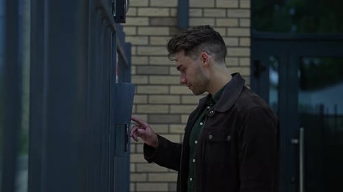 Young Man Ringing Intercom System Standing on City Street Waiting Patiently for Access to