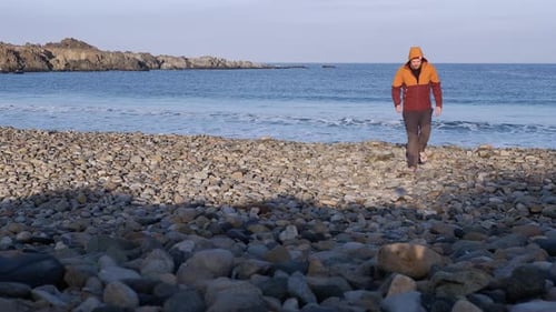 Einsamer Mann in warmer Kleidung geht am morgendlichen Felsstrand auf die Kamera zu