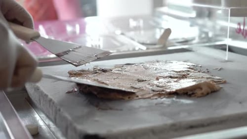 Chocolate Ice cream with cookies being spread on a cold grill with a spatula, slow motion