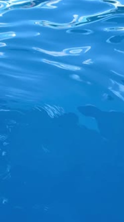 Ruhiges blaues Wasser bewegt sich sanft und erzeugt Wellen, Reflexionen des Nachmittagshimmels und das Sonnenlicht schimmern darauf.