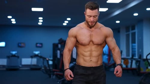 Muscle athlete strongman walks in a gym after heavy training. Perfect torso with strong abs.
