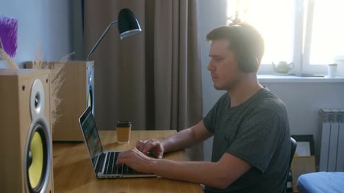 A Man in a Home Music Studio Sits at a Desk with Equipment and Looks at a Computer