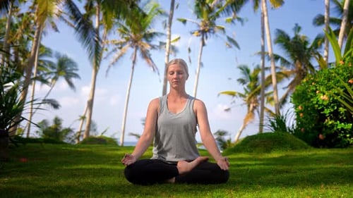 Fitness Woman Doing Yoga Exercises and Breath Meditation Sitting on Green Grass